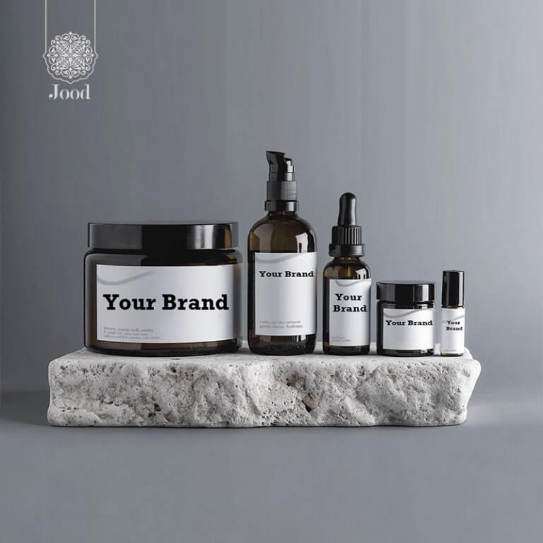 A set of minimalist skincare bottles and jars labeled 'Your Brand,' displayed on a textured stone platform with the Jood logo in the background